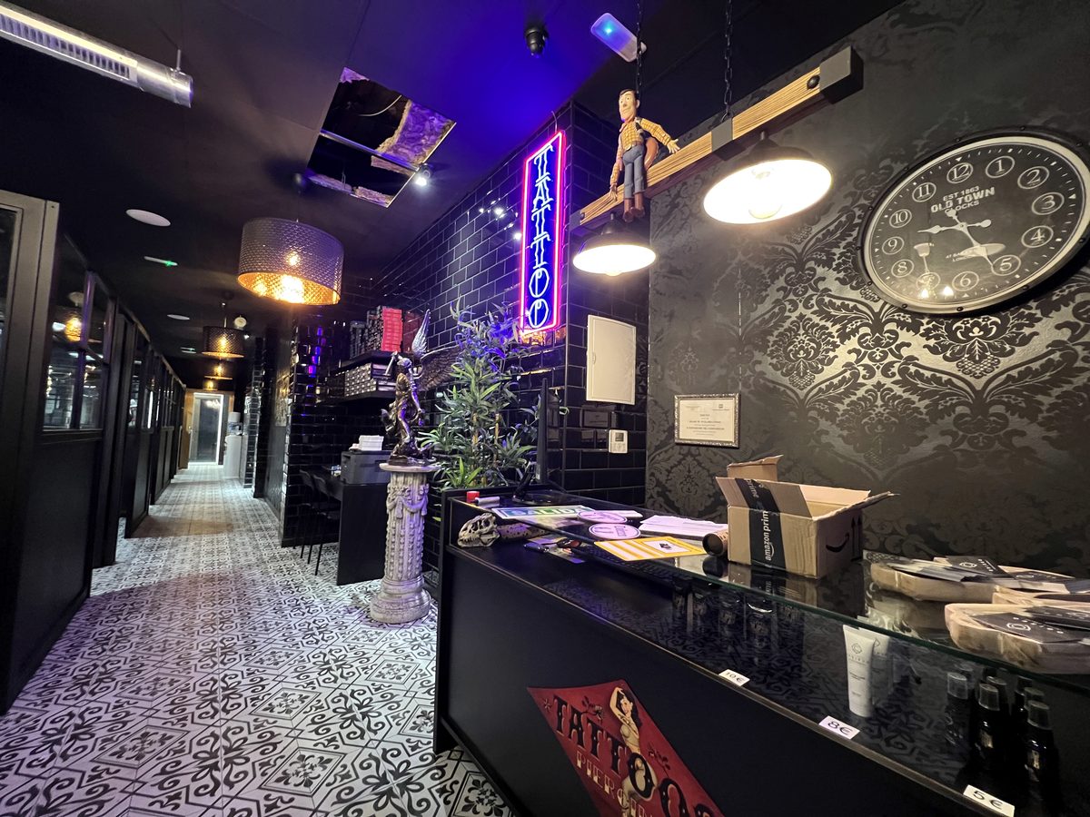 Recepción de un estudio Calipso: suelo de baldosa hidráulica en blanco y negro, azulejo de metro negro, neón de tatuaje y vitrina de joyería.